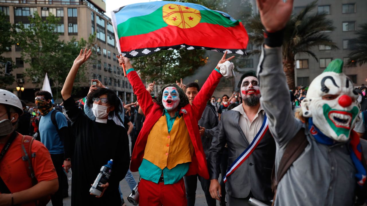 A man dressed as the Joker and holding a Mapuche flag cheers with others dressed in costumes during an anti-government protest in Santiago, Chile, Friday, Nov. 1, 2019. Chile has been facing days of unrest, triggered by a relatively minor increase in subway fares. The protests have shaken a nation noted for economic stability over the past decades, which has seen steadily declining poverty despite persistent high rates of inequality. (AP Photo/Rodrigo Abd)