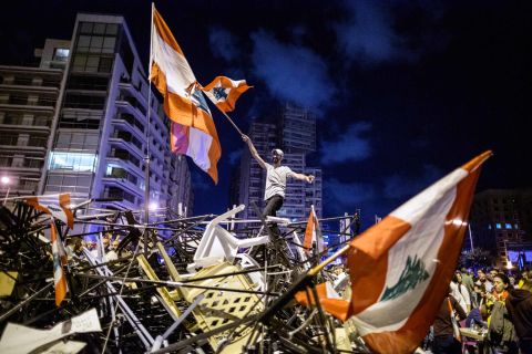 An anti-government protester waves a Lebanese flag as he stands on top of a pile of broken tents in Martyrs' Square on October 29.