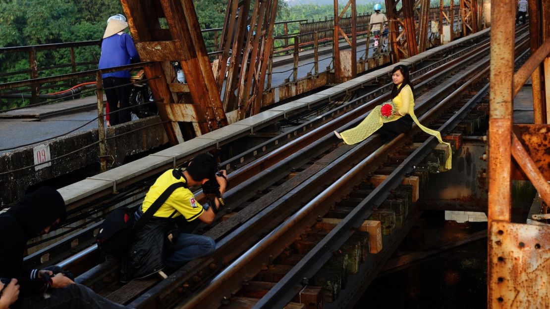 In this file photo, taken in 2014, a girl in traditional dress poses for photographs on the century-old Long Bien Bridge. According to local media, the bridge is becoming increasingly popular among travelers, too.  