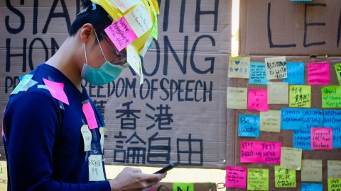 This photo taken on August 9, 2019 shows a supporter of the Hong Kong pro-democracy protests, seen covered in sticky notes, standing in front of a makeshift "Lennon Wall" at the University of Queensland in Brisbane, Australia.
