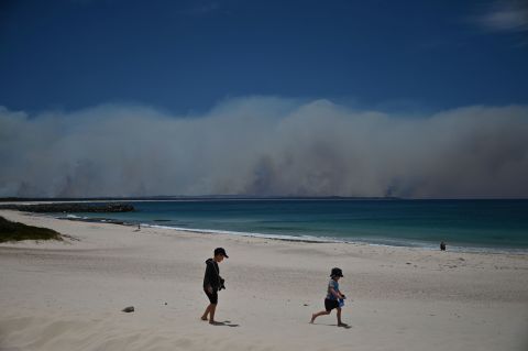 Fires burn in the distance as children play on a beach in Forster on November 9.
