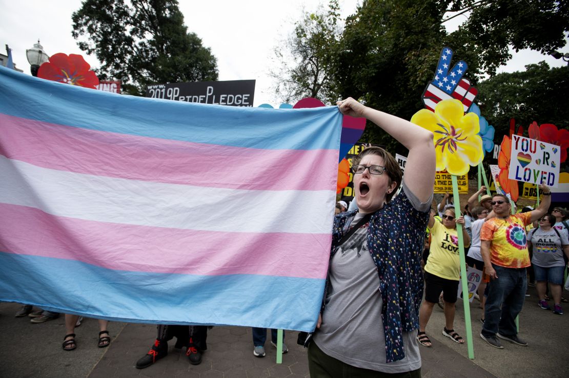 A supporter for the transgender community holds a trans flag in front of counter-protesters to protect attendees from their insults and obscenities at Atlanta's Gay Pride Festival on Saturday, October 12, 2019.