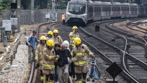 A man is escorted by firemen along train tracks near Sha Tin MTR station on November 12, 2019. 