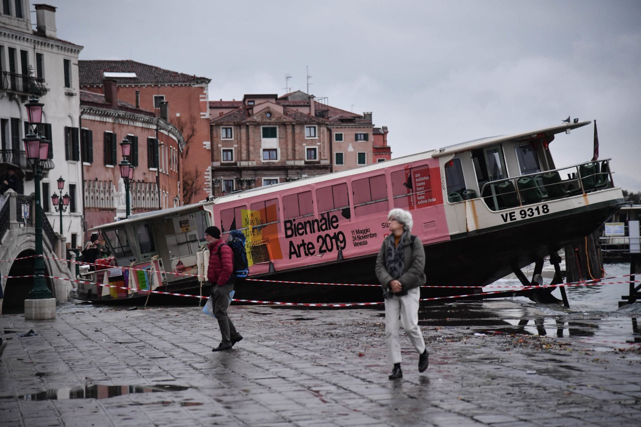 People walk past a stranded water taxi after it was washed from its mooring by the high tide.