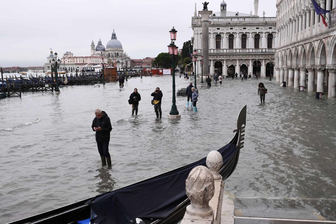 People walk past a stranded gondola across the flooded Riva degli Schiavoni embankment and St. Mark's Square in the background.
