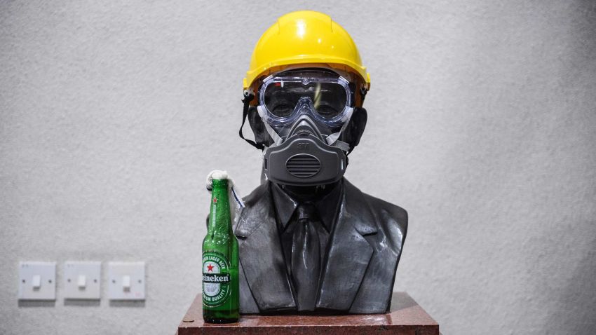 In this picture taken on November 13, 2019, a molotov cocktail, a gas mask and a yellow construction helmet are placed upon a bust of late hotel tycoon Hui Yeung Shing, who was dubbed "King of Hotels," at the campus of the