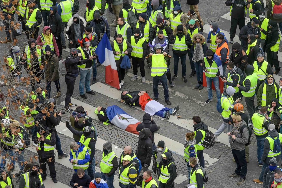 Protesters wrapped in French flags lie on the ground near riot police on the Champs Elysees on December 8, 2018.