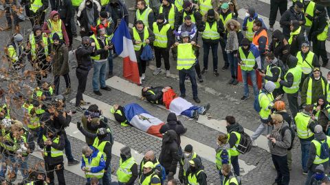 Protesters wrapped in French flags lie on the ground near riot police on the Champs Elysees on December 8, 2018.