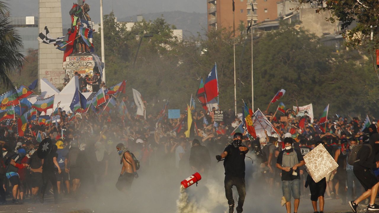 A demonstrator throws a fire extinguisher at riot police during a protest in Santiago to commemorate the first anniversary of the murder of Camilo Catrillanca, on November 14, 2019.