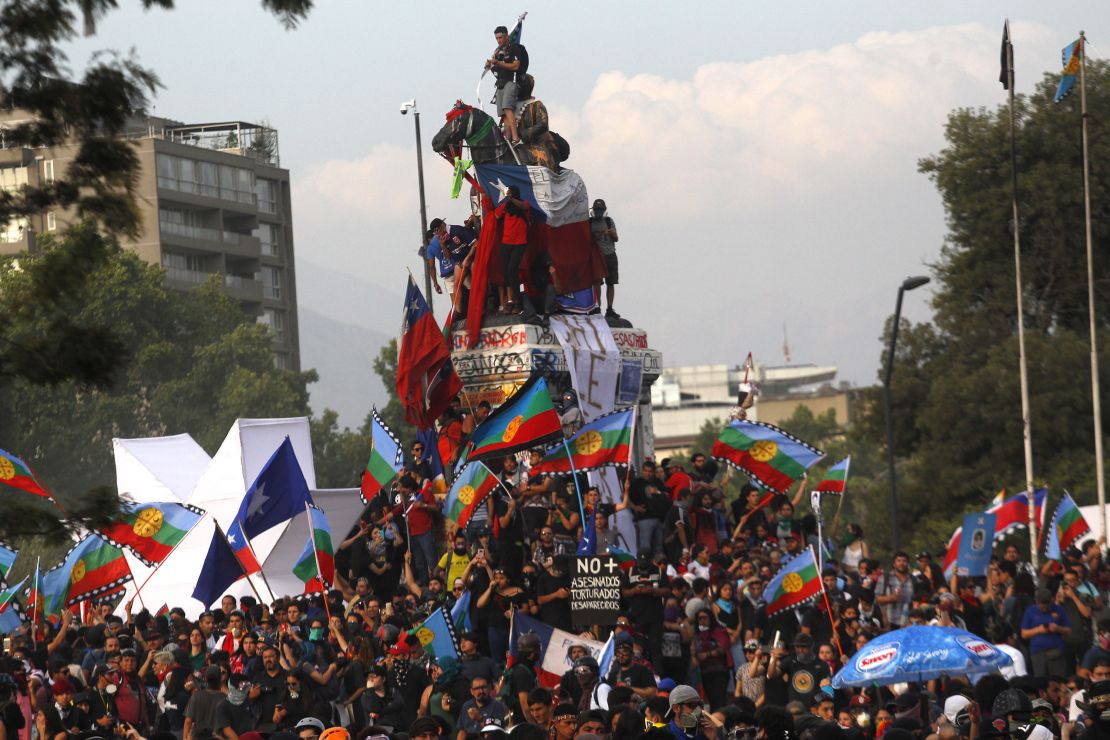 Demonstrators climb on top of a monument in Plaza Italia, Santiago during a protest against Chilean President Sebastian Pinera on November 14, 2019.