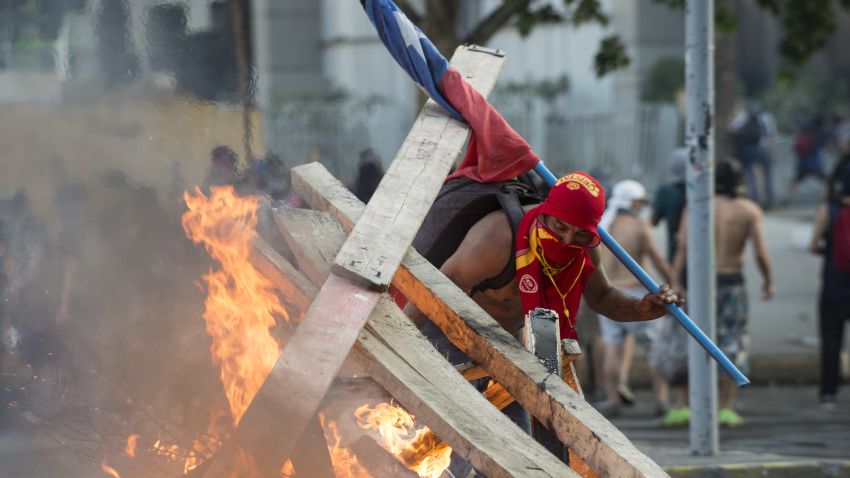 SANTIAGO, CHILE - NOVEMBER 14: A demonstrator feeds a burning barricade during a protest against president Sebastian Piñera to commemorate the first anniversary of the murder of Camilo Catrillanca November 14, 2019 in Santiago, Chile. Camilo Catrillanca, 24-year-old grandson of a prominent Mapuche leader, was shot by Chilean police exactly a year ago in the southern region of Araucanía. The murder, followed by a cover-up attempt, led to massive protests putting the spotlight in the treatment given to indigenous communities. Chile undergoes a social and political turmoil with continuous protests and looting since October 18, when a raise in the subway fare triggered rage of population. Demonstrators demand improvements in basic services and benefits, including pensions, health, and education. Piñera ordered a cabinet reshuffle and proposed changes in the national constitution but social unrest continues. (Photo by Claudio Santana/Getty Images)