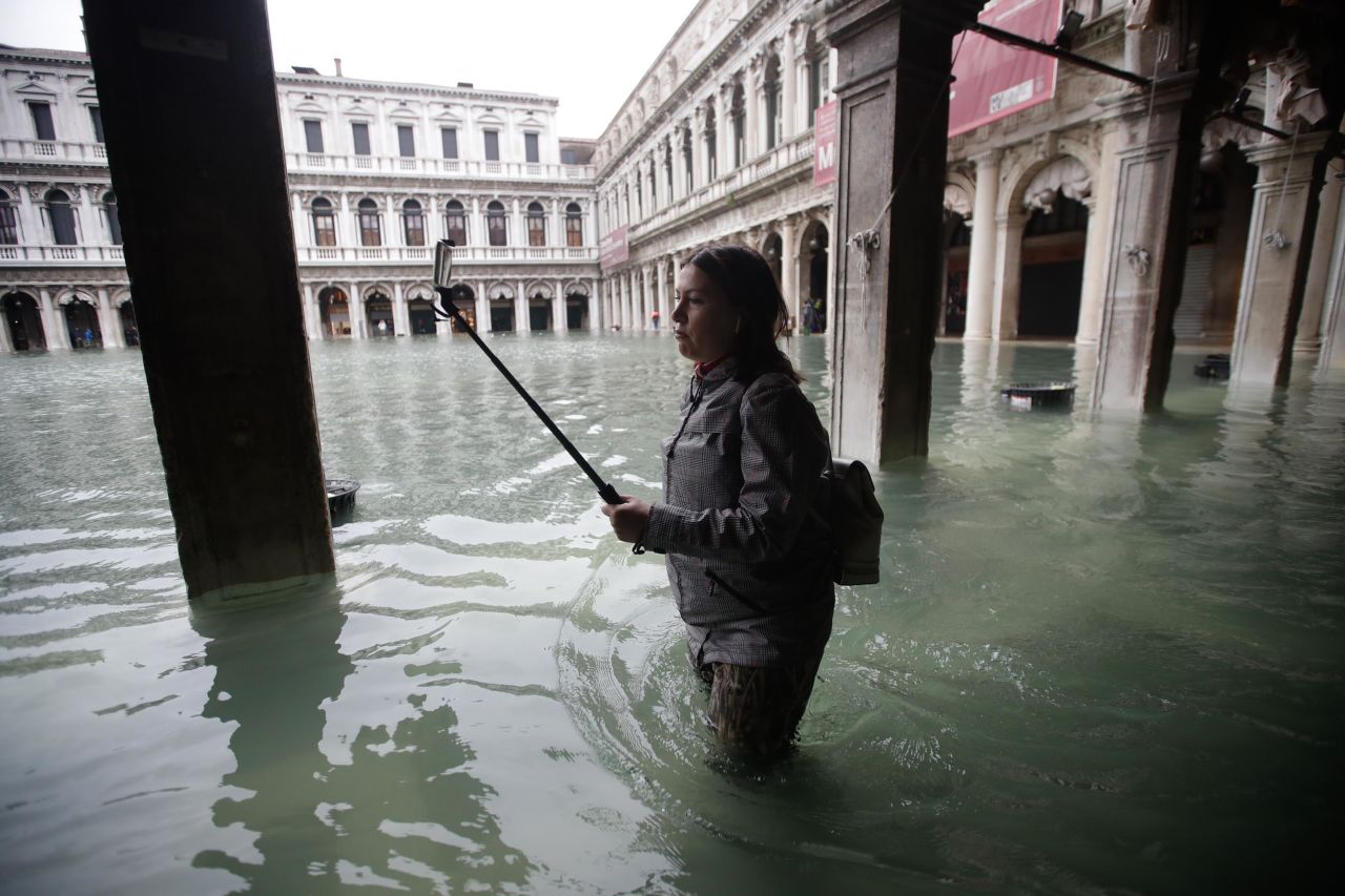 A woman with a selfie stick makes her through a flooded St. Mark's Square.