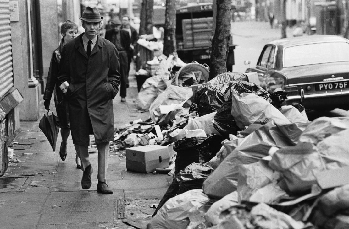 A pedestrian walks past piles of trash during a strike by sanitation workers in 1970.