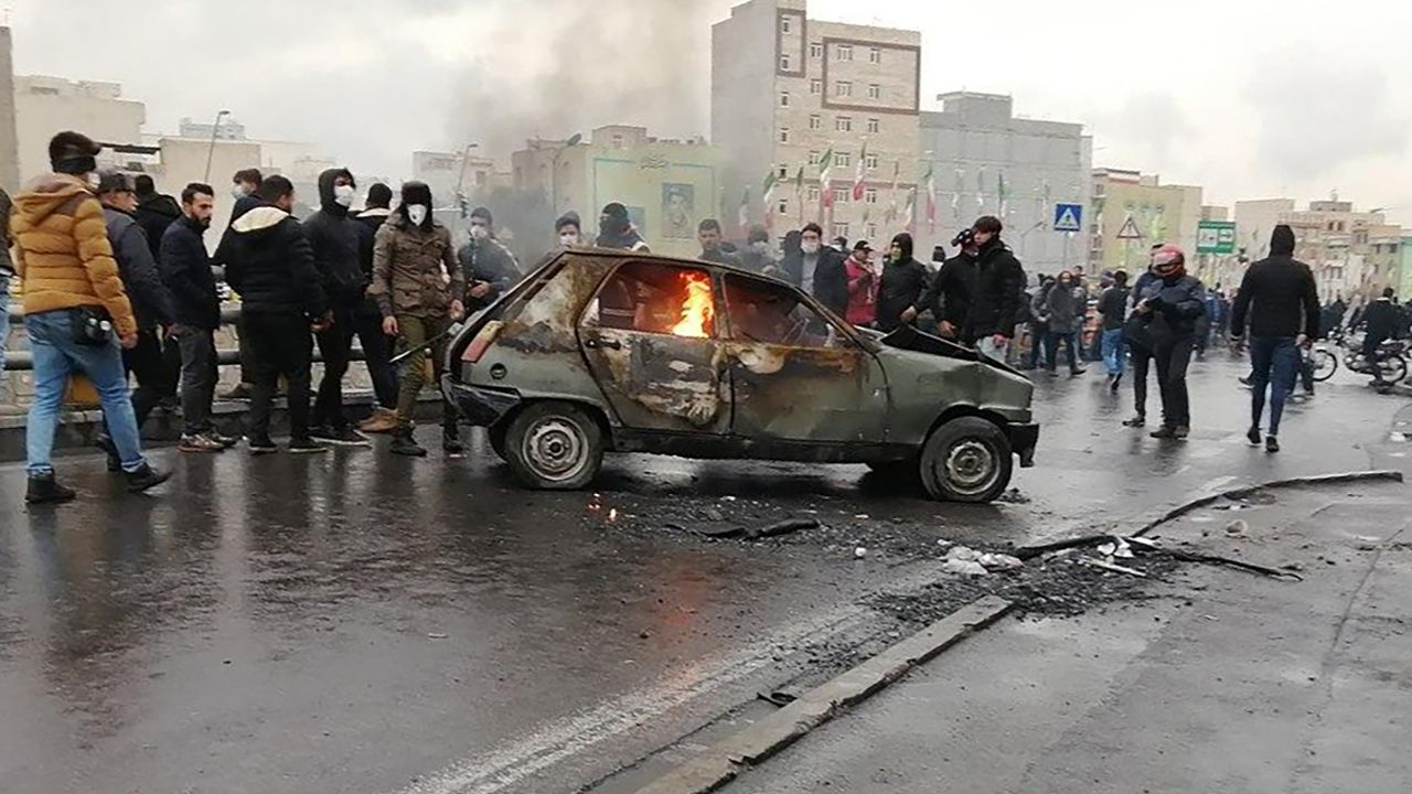 Iranian protesters gather around a burning car Saturday in the capital city of Tehran.
