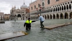 A city worker helps a woman who decided to cross St. Mark square on a gangway, in spite of prohibition, in Venice, Italy, Sunday, Nov. 17, 2019. Venetians are bracing for the prospect of another exceptional tide in a season that is setting new records. Officials are forecasting a 1.6 meter (5 feet, 2 inches) surge Sunday. That comes after Tuesday's 1.87 meter flood, the worst in 53 years, followed by high tide of 1.54 meters on Friday. (AP Photo/Luca Bruno)