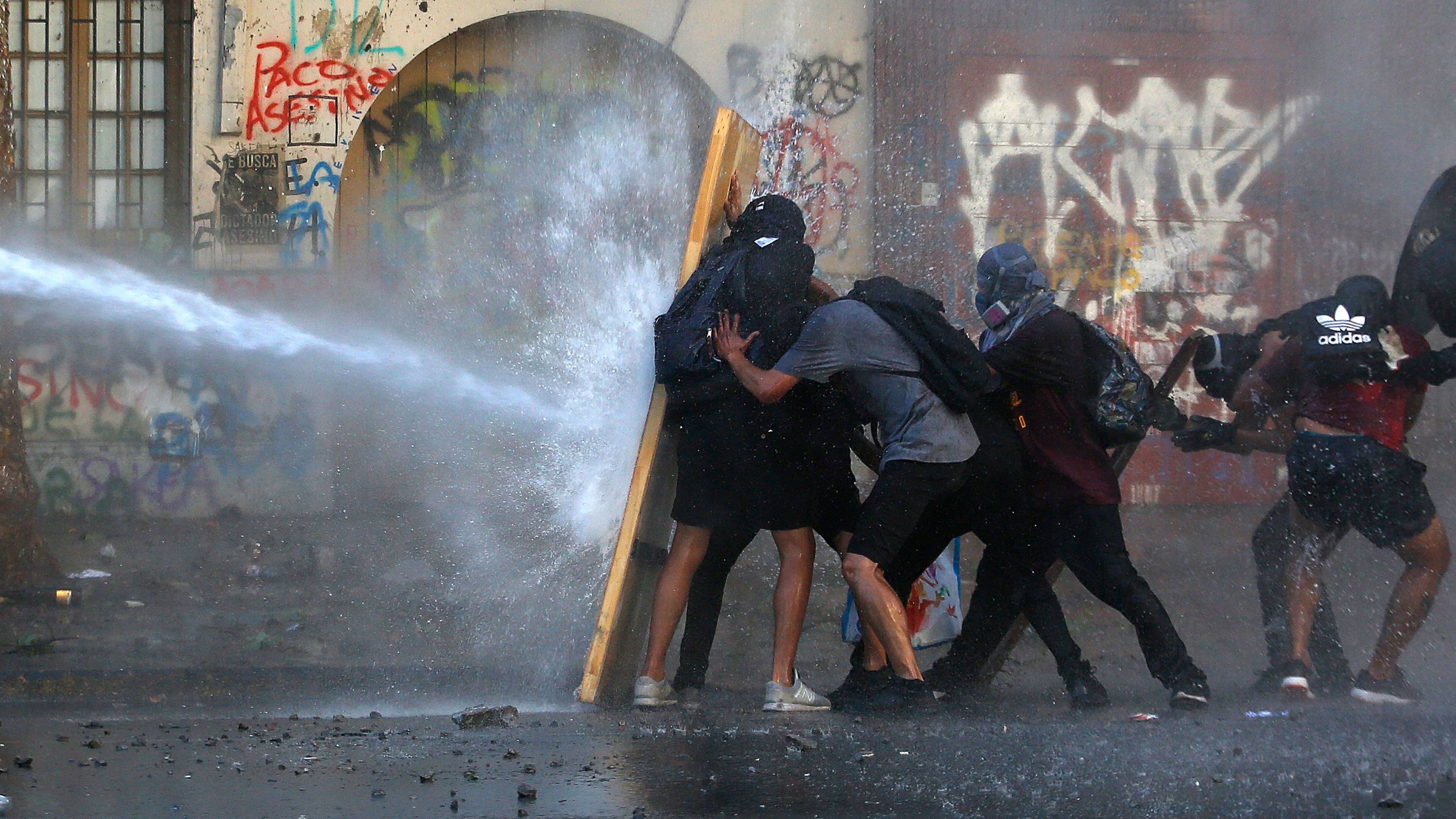 Demonstrators take cover from water fired by a riot police truck during a protest against President Sebastian Piñera on November 19 in Santiago, Chile.