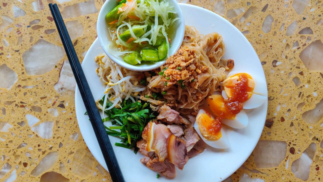 <strong>Mi kola (Kola noodles): </strong>The Kola are an ethnic minority in Cambodia. Kola noodles are garnished with dried shrimp, hard-boiled egg slices, cucumbers, peanuts, and fresh herbs and mixed with a tangy lime-garlic-shallot dressing.