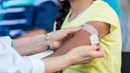 Unrecognizable female doctor applies an adhesive bandage to preteen girl's arm after the girl receives a flu shot at an outdoor free clinic.