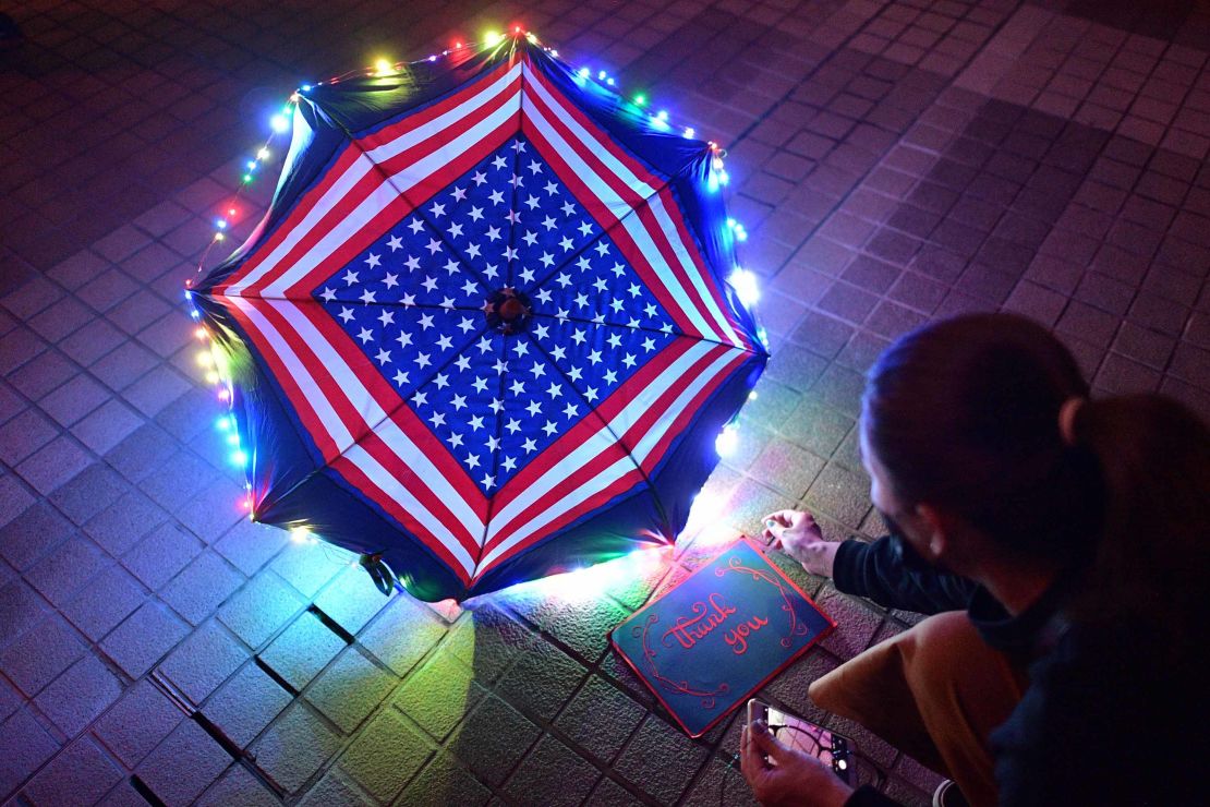 A protester sits beside a thank you note and an umbrella bearing patterns of the US flag.