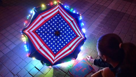 A protester sits beside a thank you note and an umbrella bearing patterns of the US flag.