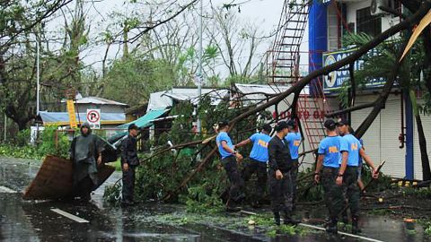 Policemen remove branches from a damaged tree following the passage of Typhoon Kammuri south of Manila.