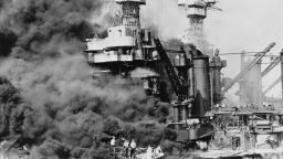 Pearl Harbor, Hawaii. A small boat rescues a seaman from the 31,800 ton USS West Virginia burning in the foreground. Smoke rolling out amidships shows where the most extensive damage occurred. Note the two men in the superstructure. The USS Tennessee is inboard