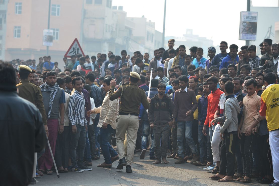 Police personnel try to clear a road as onlookers gather near the factory fire.
