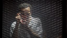 FILE - In this July 28, 2018 file photo, Egyptian photojournalist Mahmoud Abu Zied, known by his nickname Shawkan, gestures in a soundproof glass cage inside a makeshift courtroom in Tora prison in Cairo. Egypt has created a new high-powered human rights watchdog agency, but its primary mission isn't to protect Egyptians from violations. Instead, the body is primarily aimed at protecting the government from allegations of rights abuses, especially those made by international groups. The new body reflects an attitude of the state under President Abdel-Fattah el-Sissi that sees accusations of human rights violations to be intended to undermine the government and cause instability. (AP Photo/Amr Nabil, File)