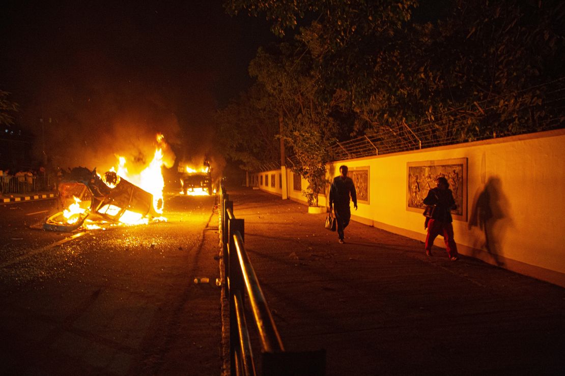 People walk past vehicles set on fire by demonstrators protesting against the Citizenship Amendment Bill (CAB) in Guwahati, India, Wednesday, December 11, 