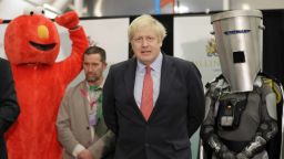 Bobby Smith, a political and fathers' rights activist and founder and leader of the 'Give Me Back Elmo' party, left, and Independent candidate Count Binface stand either side of Britain's Prime Minister and Conservative Party leader Boris Johnson wait for the Uxbridge and South Ruislip constituency count declaration at Brunel University in Uxbridge, London, Friday, Dec. 13, 2019. (AP Photo/Kirsty Wigglesworth)