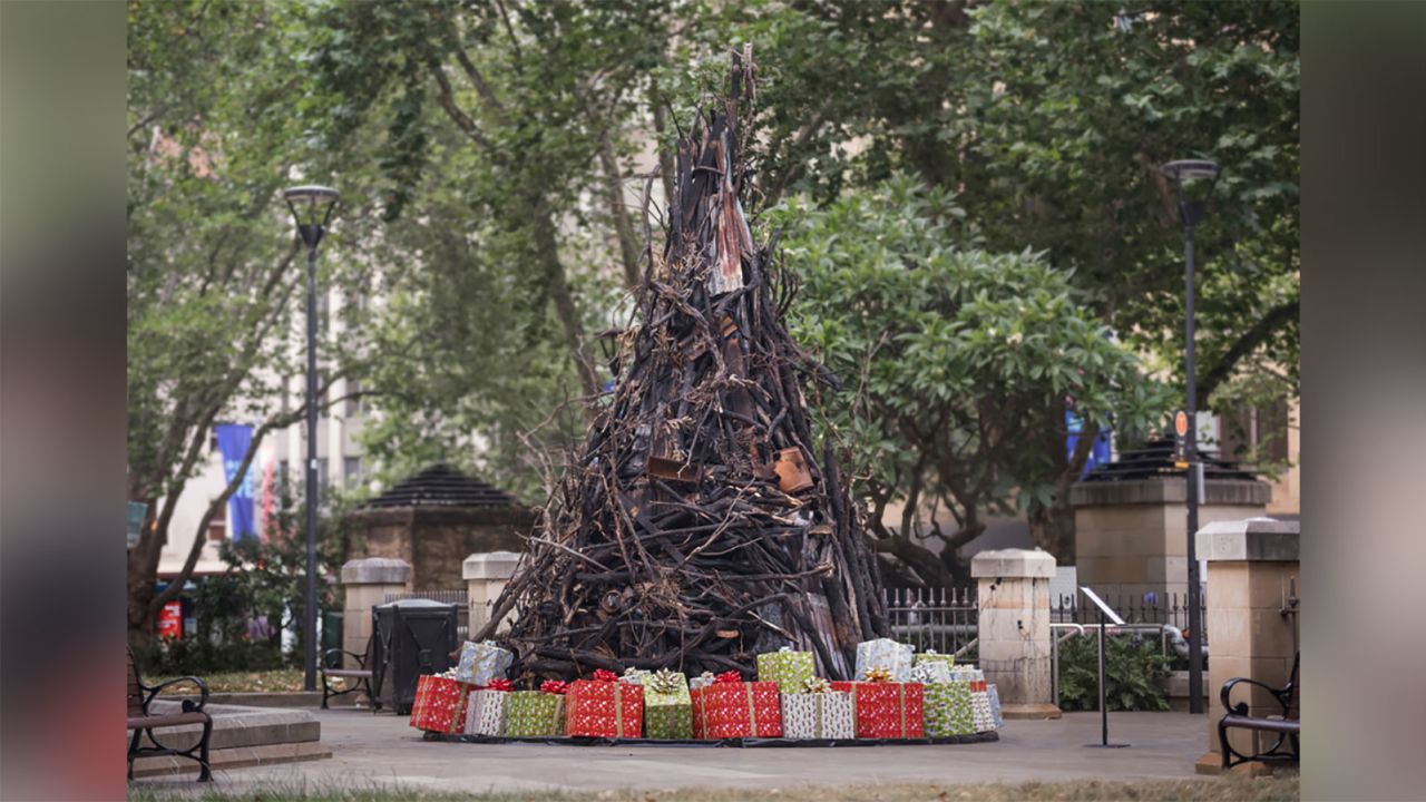 An installation of a charred Christmas tree on display in Wynward Park, downtown Sydney, created by artist James Dive. The tree is constructed out of charred logs and burnt household items gathered from the aftermath of bush fires that have scorched the region.