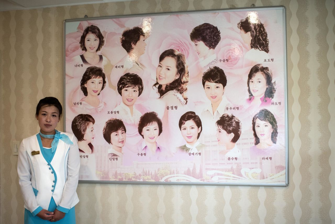 A staff poses next to a board displaying approved hairstyles at a women's salon in the Munsu Water Park complex in Pyongyang, North Korea in 2018.