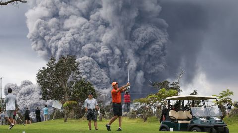 People play golf on Hawaii's Big Island as an ash plume from the Kilauea volcano rises in the distance. <a href="https://www.cnn.com/interactive/2018/05/us/hawaii-kilauea-volcano-eruption-cnnphotos/" target="_blank">The volcano erupted in May 2018,</a> sending a smoldering flow of lava into residential areas.