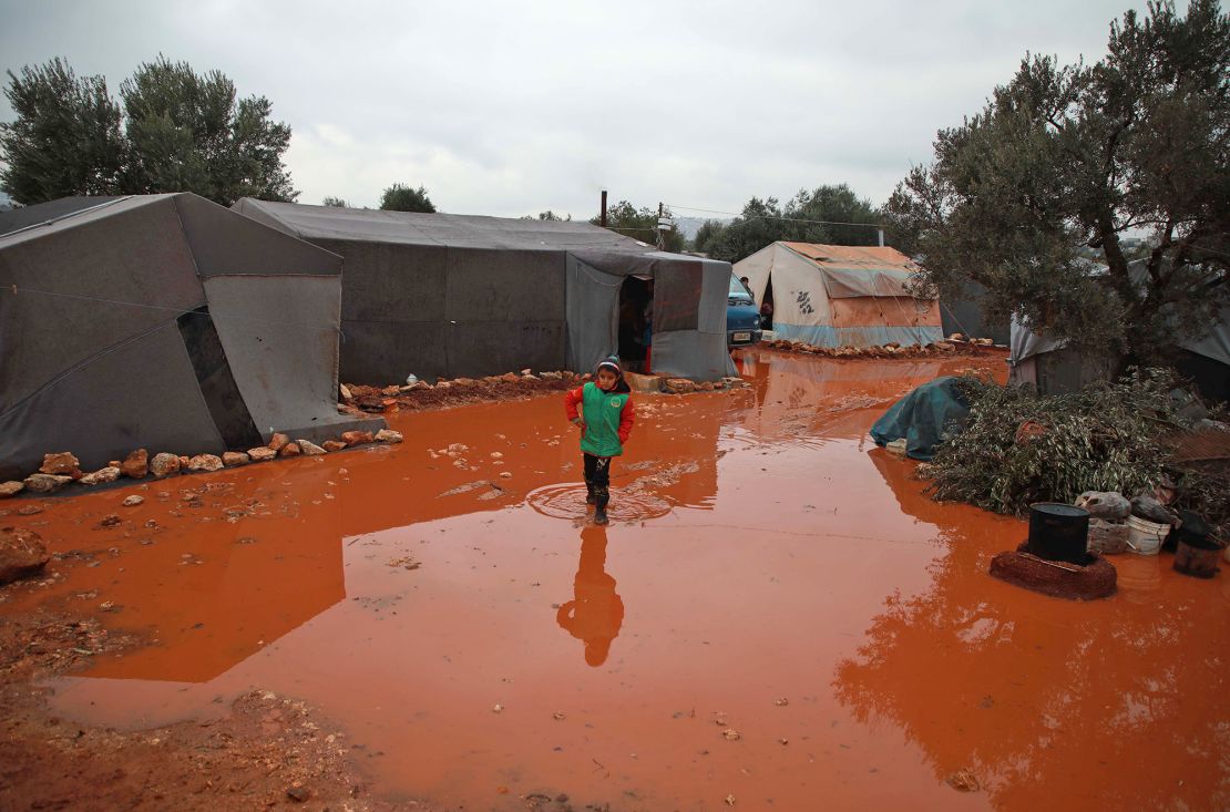 A girl walks through a rainwater puddle before tents in a flooded camp for displaced Syrians near the village of Killi in northwestern Idlib province on December 5, 2019.
