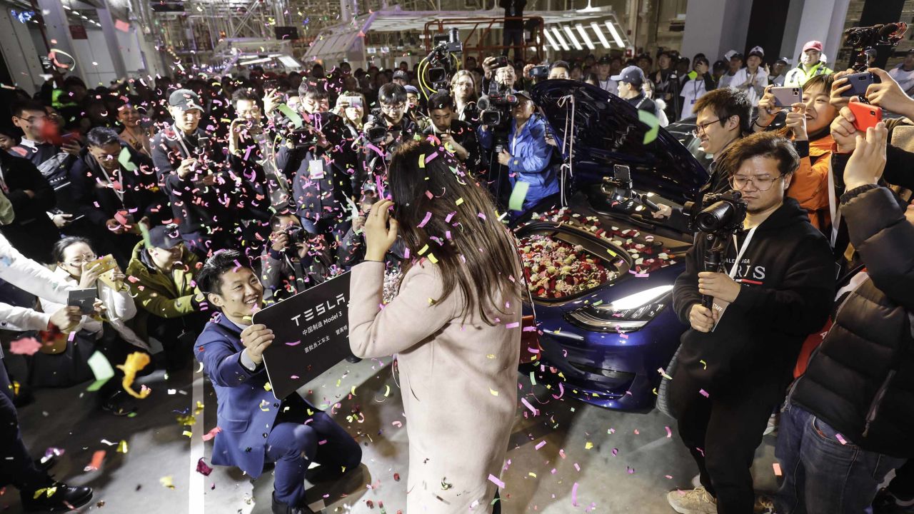 An employee, left, proposes to his girlfriend with his newly delivered Tesla Model 3 in Shanghai on Monday.