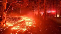 TOPSHOT - Burning embers cover the ground as firefighters (back R) battle against bushfires around the town of Nowra in the Australian state of New South Wales on December 31, 2019. - Thousands of holidaymakers and locals were forced to flee to beaches in fire-ravaged southeast Australia on December 31, as blazes ripped through popular tourist areas leaving no escape by land. (Photo by Saeed KHAN / AFP) (Photo by SAEED KHAN/AFP via Getty Images)