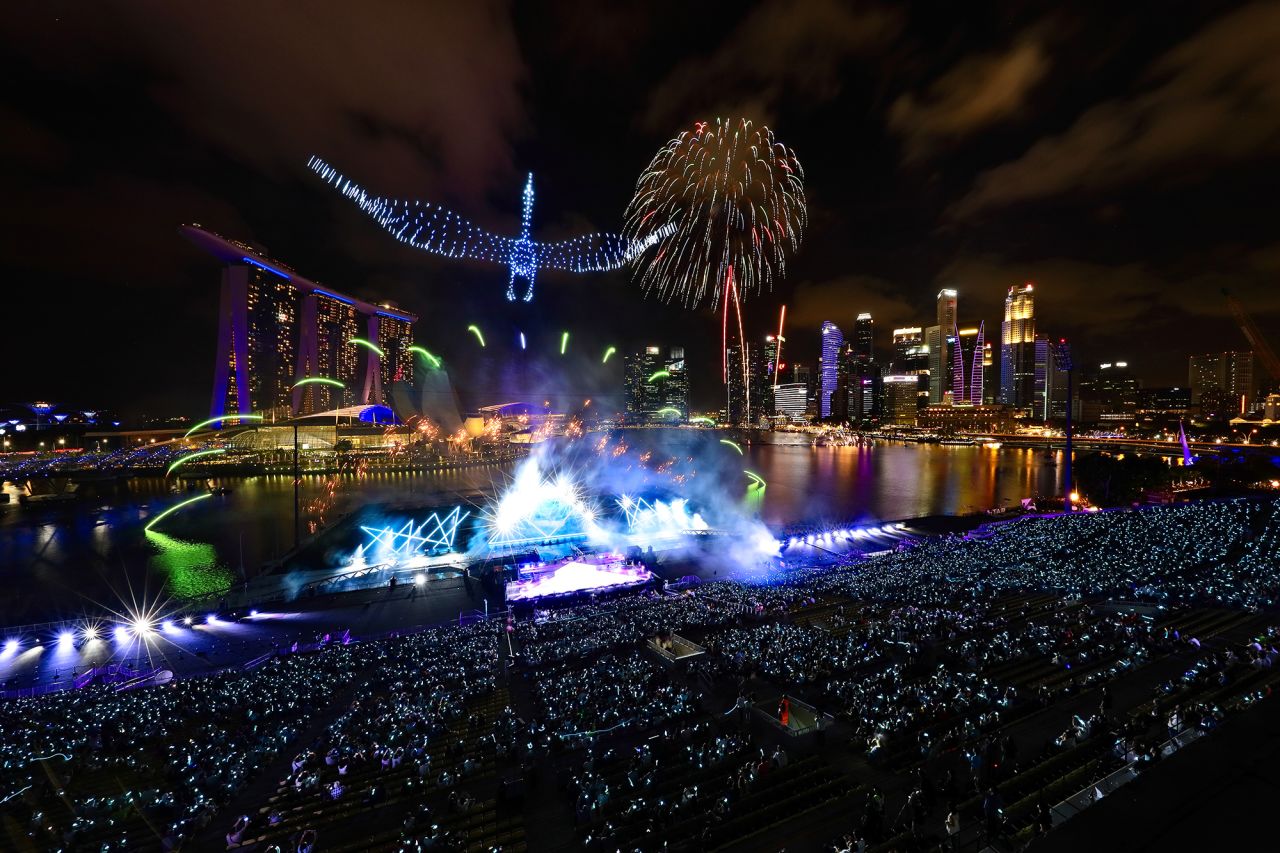 Drones form the shape of a crane in the sky as fireworks erupt at Singapore's Marina Bay.