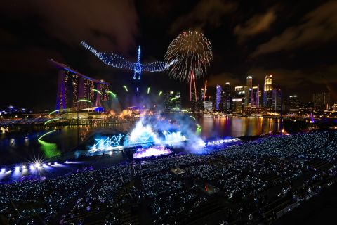 Drones form the shape of a crane in the sky as fireworks erupt at Singapore's Marina Bay.