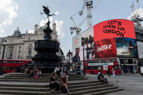 People sit in Piccadilly Circus as the light display reads 'Let's Open Up London' on the day of lifting of nearly all remaining coronavirus restrictions in London, on July 19.