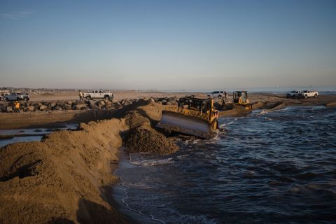 Excavators dredge sand to block some of the oil from flowing into Huntington Beach.