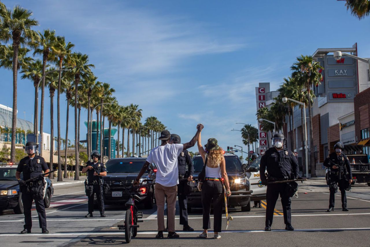 A black man and a white woman hold their hands up in a front of police officers in downtown Long Beach on May 31, 2020 during a protest against the death of George Floyd.