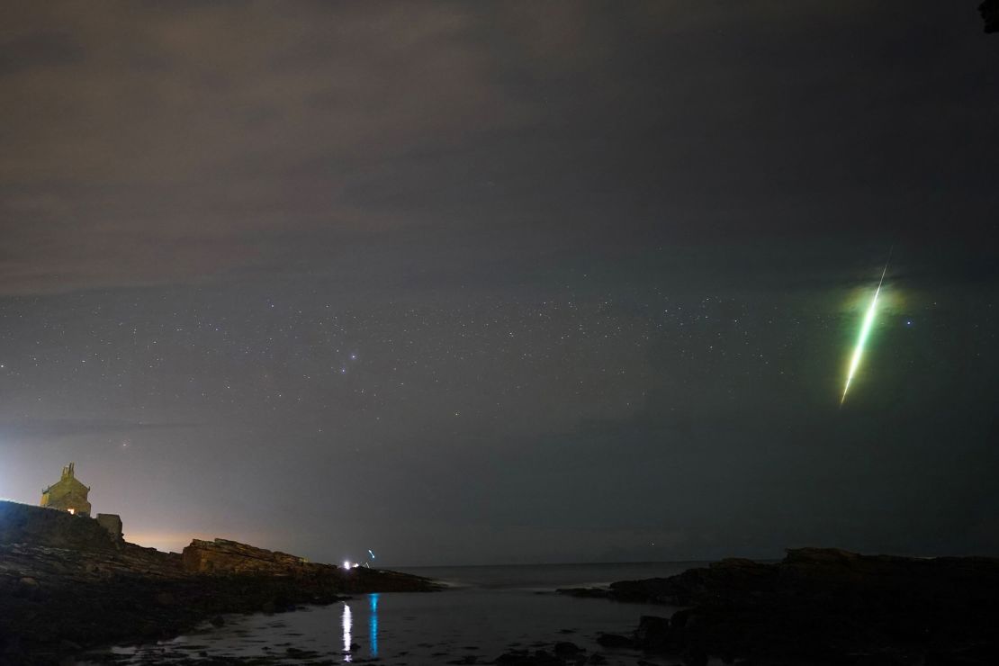 A meteor streaks across the sky during the Draconid meteor shower as seen over Howick rocks in Northumberland in northeast England in October 2021.