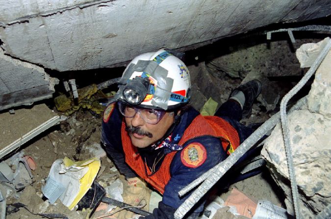 A firefighter crawls through a tight crevice deep inside the rubble of the bombed building.