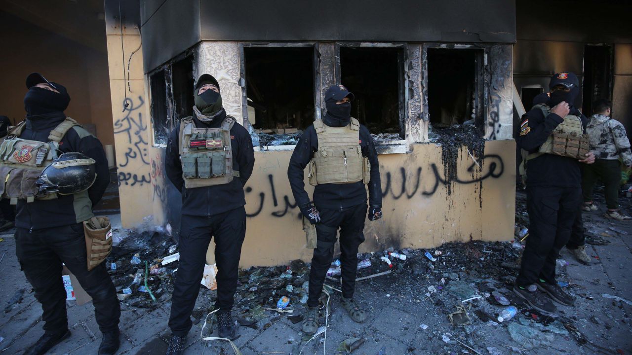 Iraqi security forces gather at the entrance of the US embassy in the Iraqi capital Baghdad on January 1, 2020, as smoke billows following a demonstration by supporters of the largely Iranian-trained Hashed al-Shaabi paramilitary force. - Thousands of Iraqi supporters of the largely Iranian-trained Hashed al-Shaabi paramilitary force had gathered at the embassy, outraged by US strikes that killed 25 Hashed fighters over the weekend. They marched unimpeded through the checkpoints of the usually high-security Green Zone to the embassy gates, where they broke through a reception area, chanting "Death to America" and scribbling pro-Iran graffiti on the walls. (Photo by AHMAD AL-RUBAYE / AFP) (Photo by AHMAD AL-RUBAYE/AFP via Getty Images)