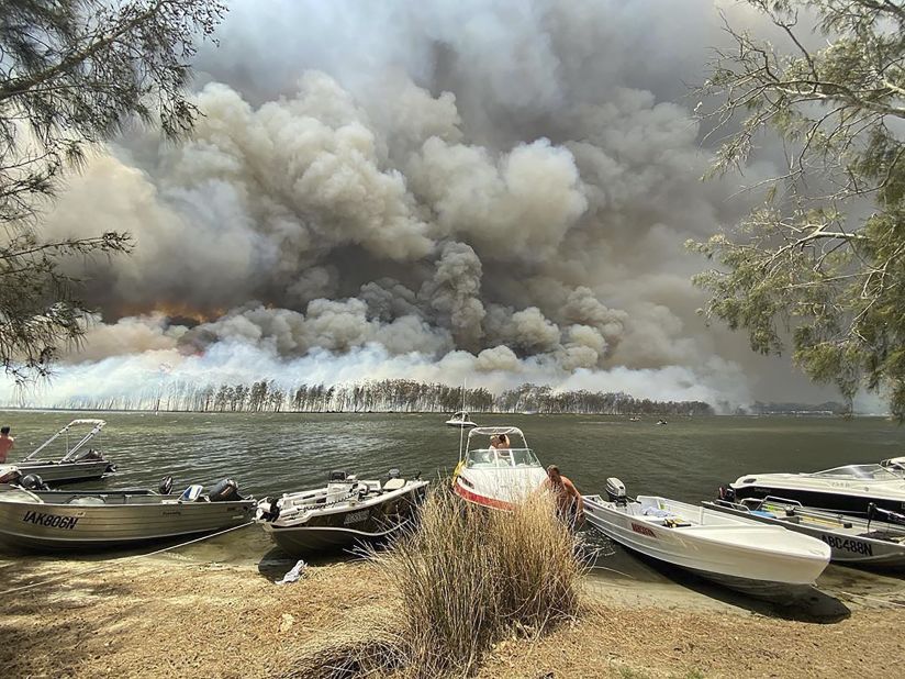 Boats are pulled ashore as smoke and wildfires rage on January 2 behind Lake Conjola.