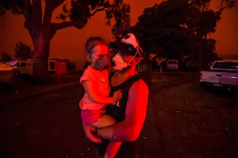 A father holds his daughter as the skies above turn red during the day on January 4 in Mallacoota, Australia. Many parents with young children were stuck in Mallacoota after flights were grounded because of smoke and only school-aged children and older were allowed to evacuate by boat. 