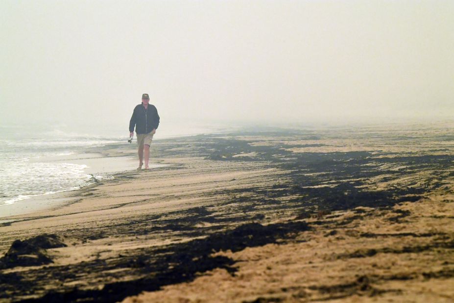 A man walks past ash from bushfires washed up on a beach in Merimbula on January 5.