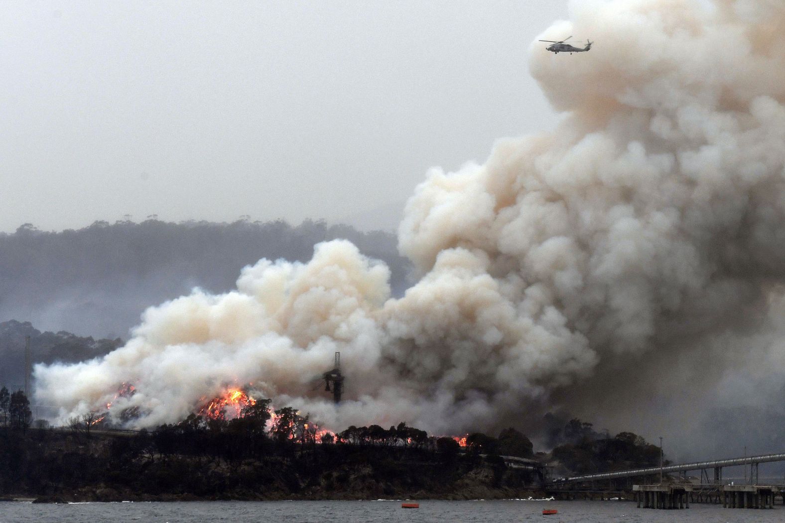 A military helicopter flies above a burning woodchip mill in Eden, New South Wales, on January 6.