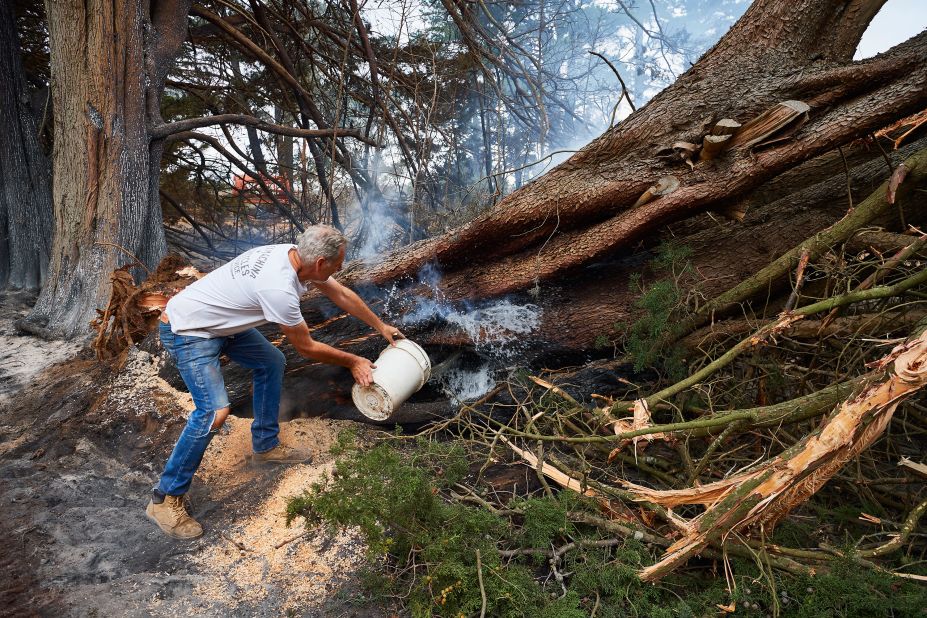 A resident throws a bucket of water onto a smoldering tree on his property on Monday, January 6, in Wingello, Australia. 