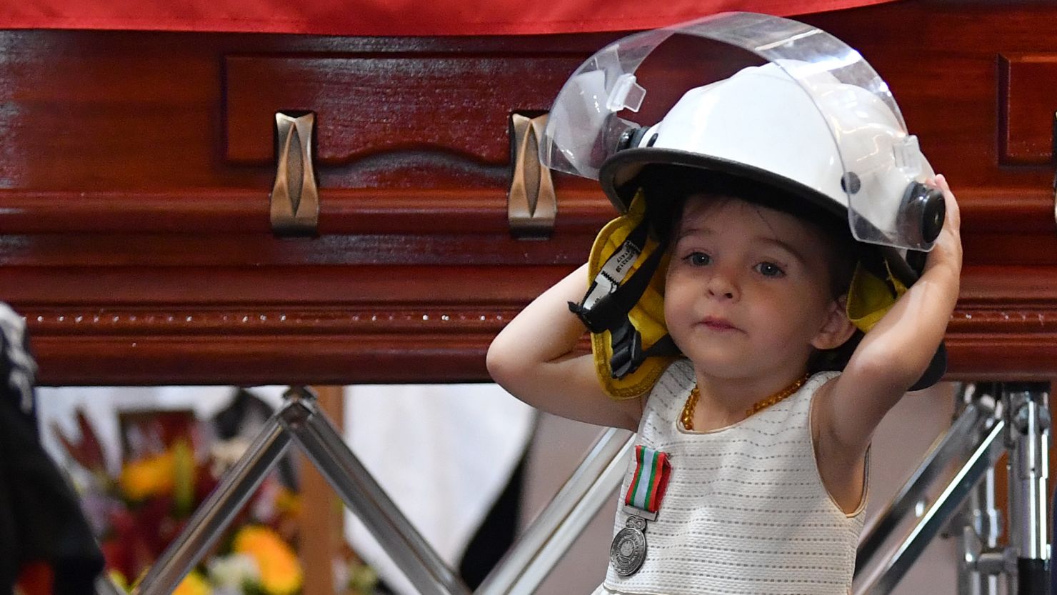 Charlotte O'Dwyer, the young daughter of Rural Fire Service volunteer Andrew O'Dwyer, stands in front of her father's casket wearing his helmet.